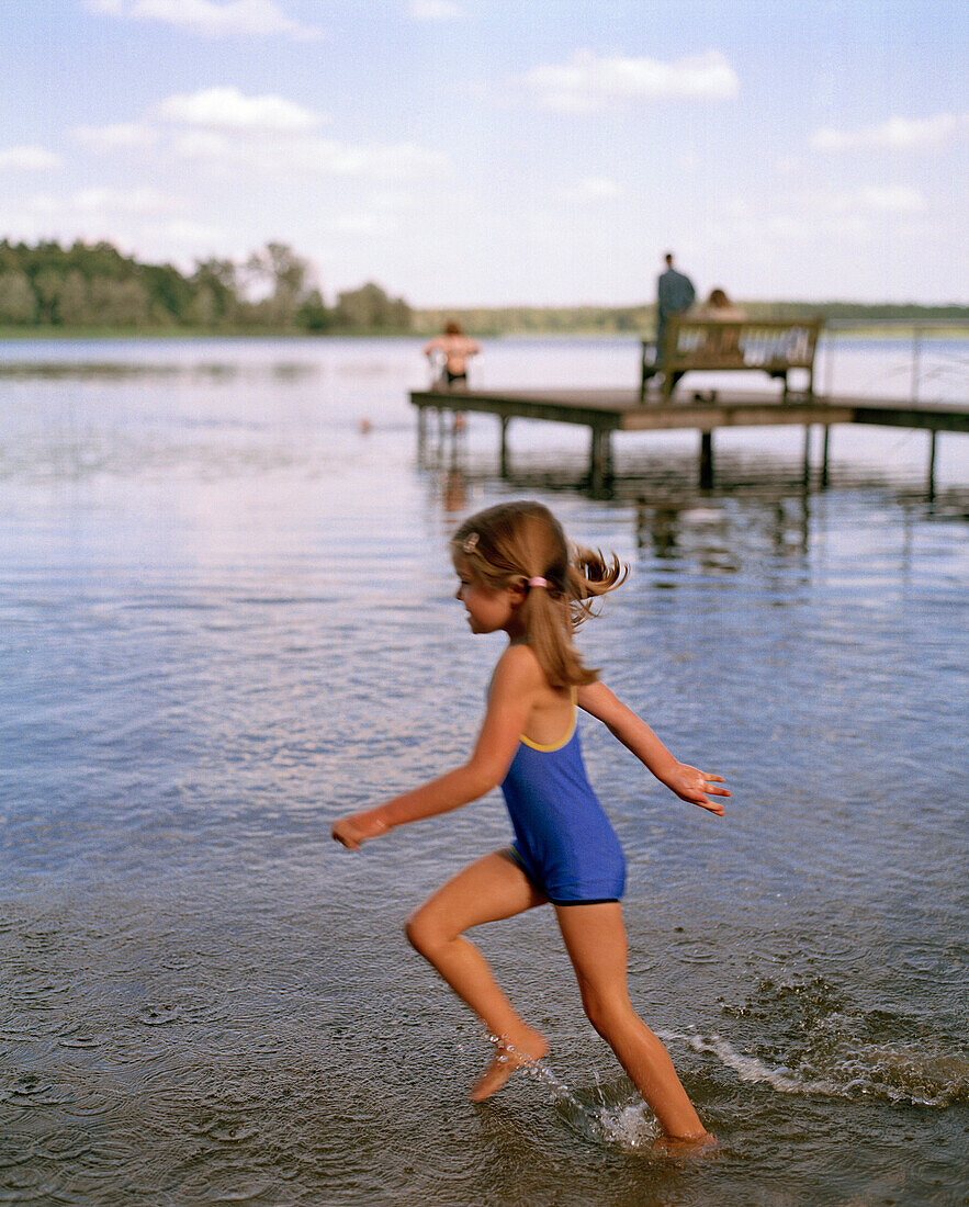 Girl (5 years) walking throug water at lakeshore, Lake Neukloster, Nakenstrof, Mecklenburg-Western Pomerania, Germany, MR, PR