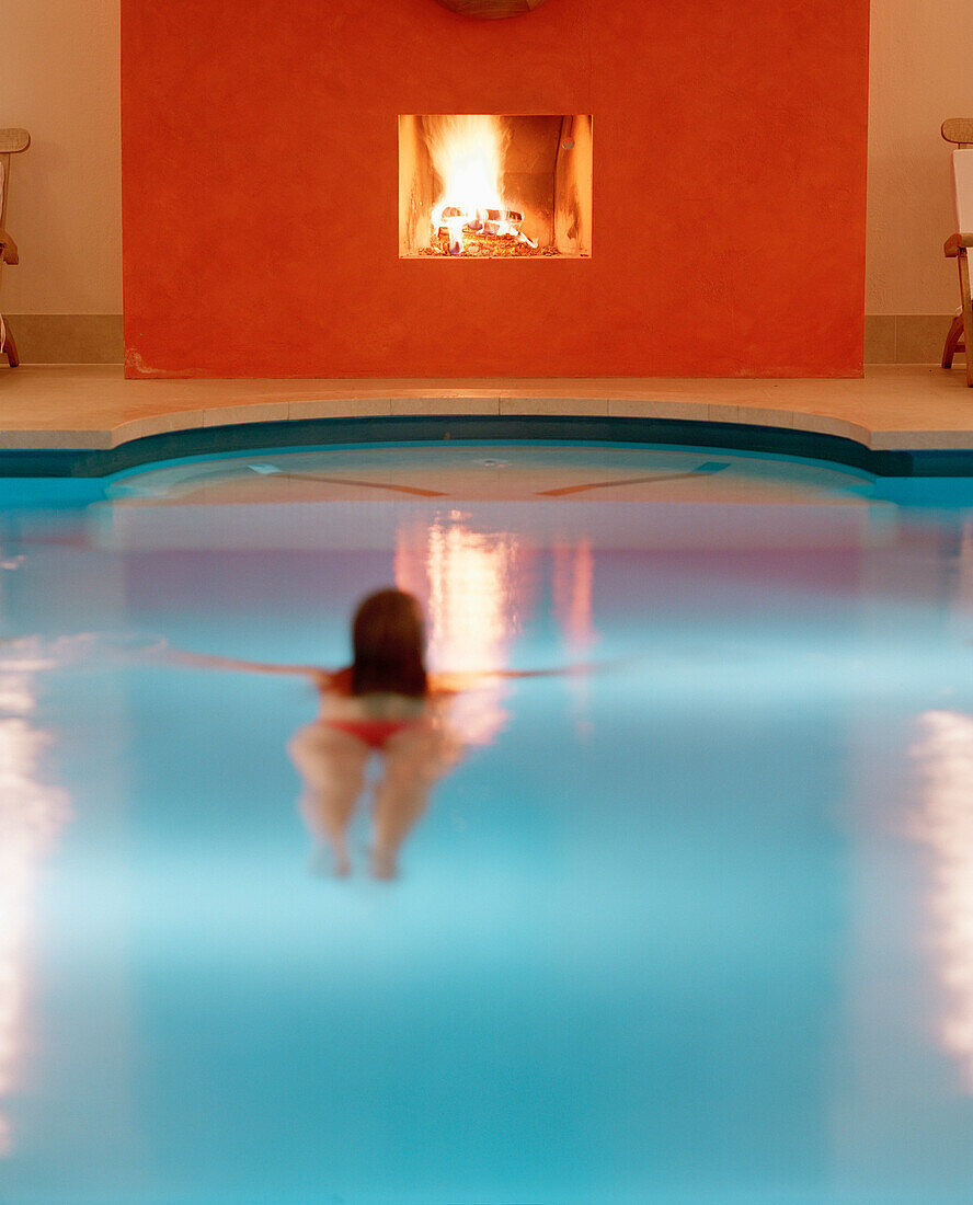 Frau schwimmt in einem Schwimmingpool, brennender Kamin im Hintergrund, Seehotel Neuklostersee, Nakenstorf, Mecklenburg-Vorpommern, Deutschland, MR, PR