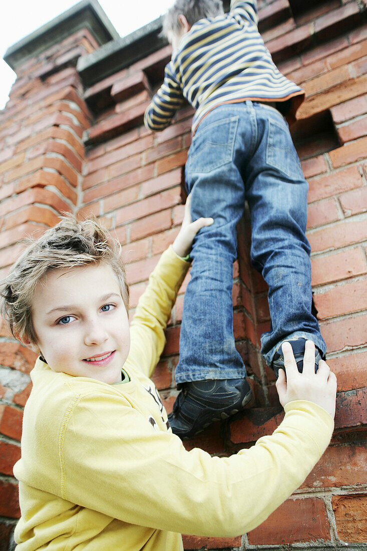 Boy giving friend a bunk-up over a wall