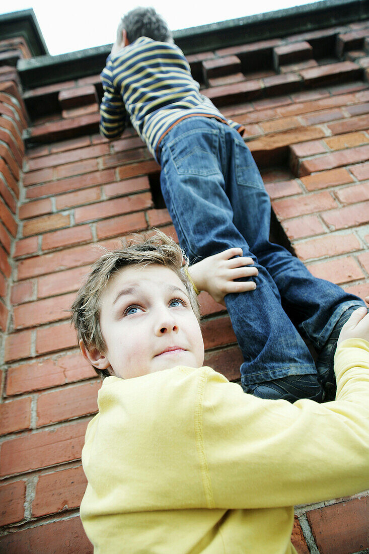 Zwei Buben klettern über Mauer, Kinder, Freizeit, Erziehung