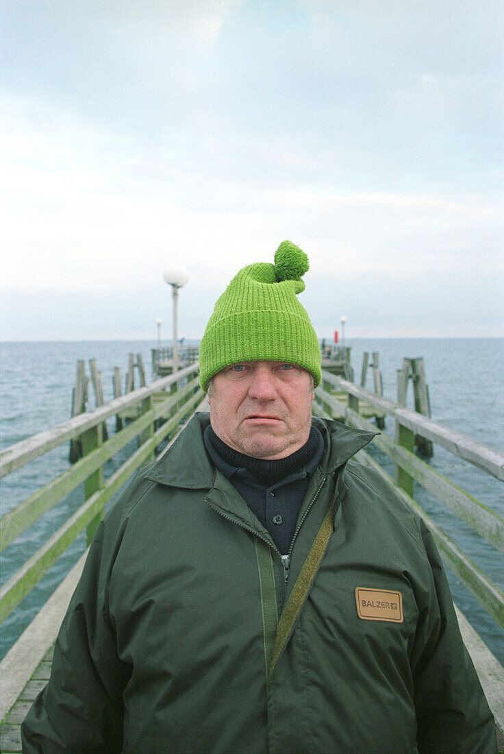 fisherman at the Baltic sea, Germany, portrait, people from germany, german, man with cap, man with pompom hat, pompom hat, green pompon hat, direct view, direct look in the camera, straight look in the camera, grim, a grimmer man, grimmer look, headgear,