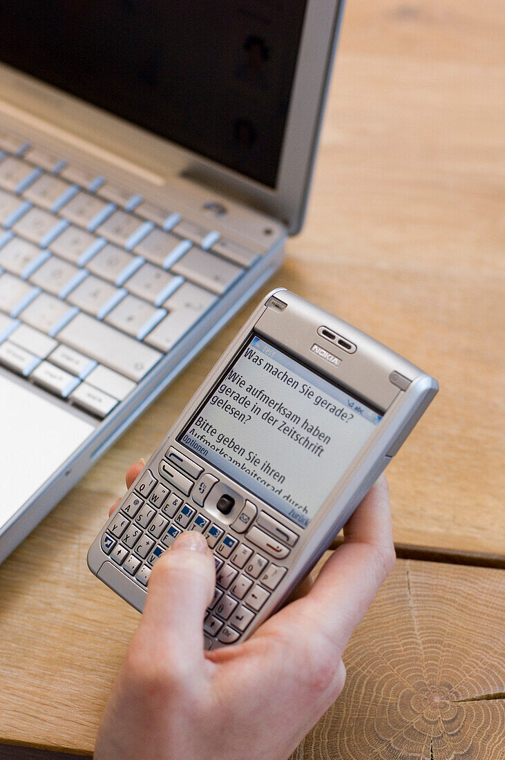 Frauenhand mit Handy und Laptop