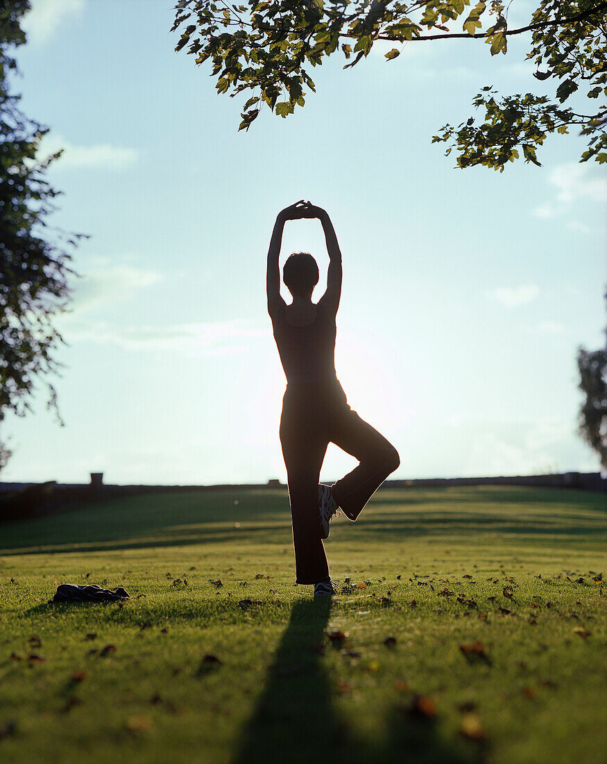 Woman relaxing doing a yoga excercise in the park area of a Wellness Hotel at sunset, near Hameln, Lower Saxony, germany