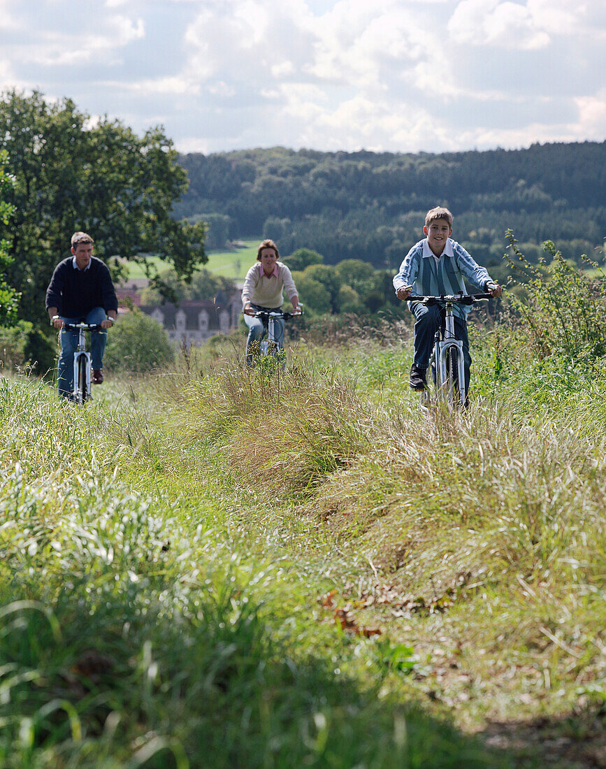 J unge, sportliche Familie mit Sohn, Fahrradtour auf einem Wiesenweg, im Hintergrund das Schloßhotel Münchhausen, bei Hameln, Weserbergland, Niedersachsen, Deutschland