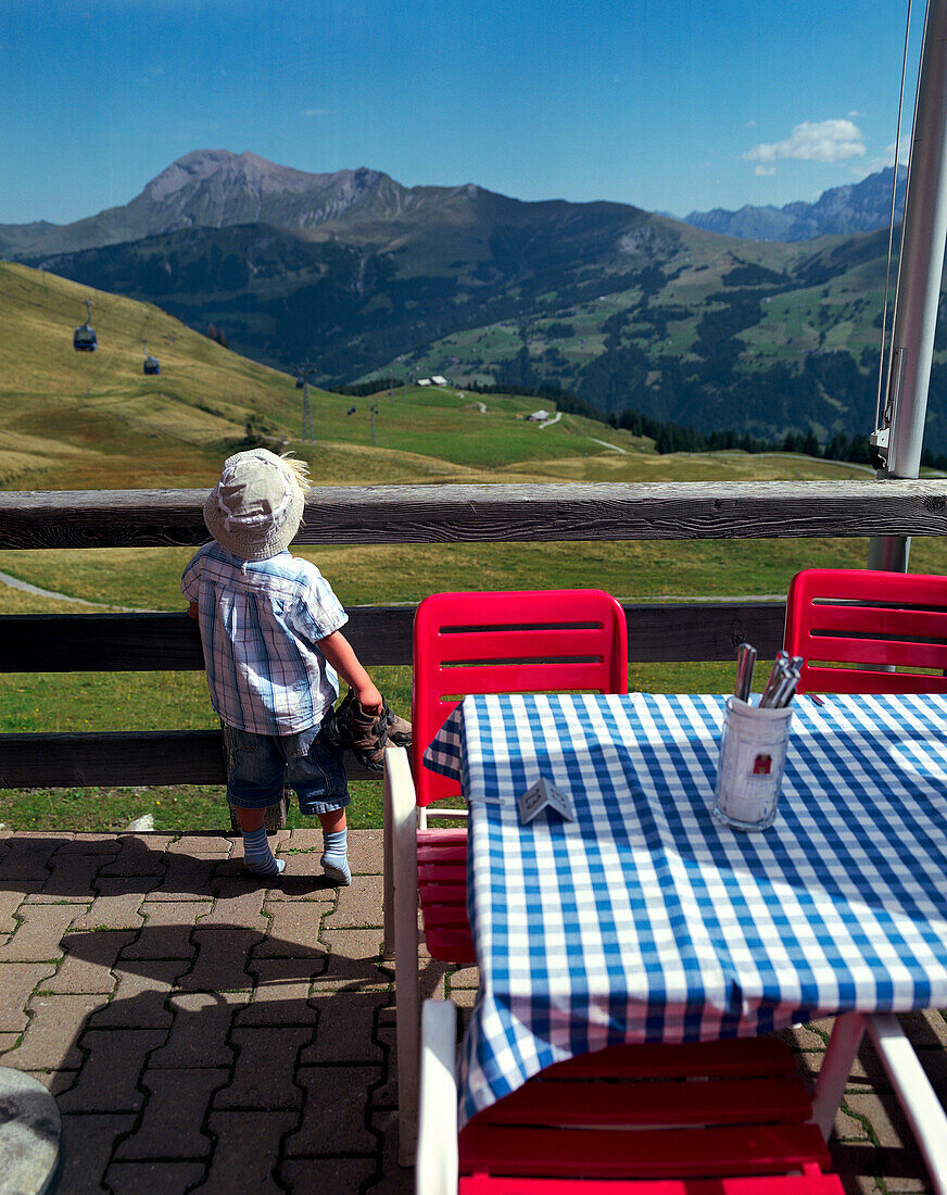 Junge steht auf einer Terrasse einer Berghütte, Simmental, Berner Alpen, Kanton Bern, Schweiz