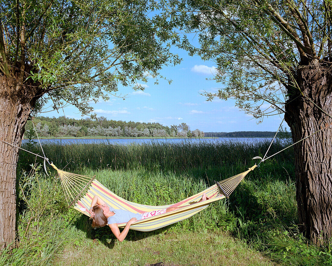 Woman lying in a hammock at lakeshore, Hotel Neuklostersee, Nakenstorf, Mecklenburg-Western Pomerania, Germany