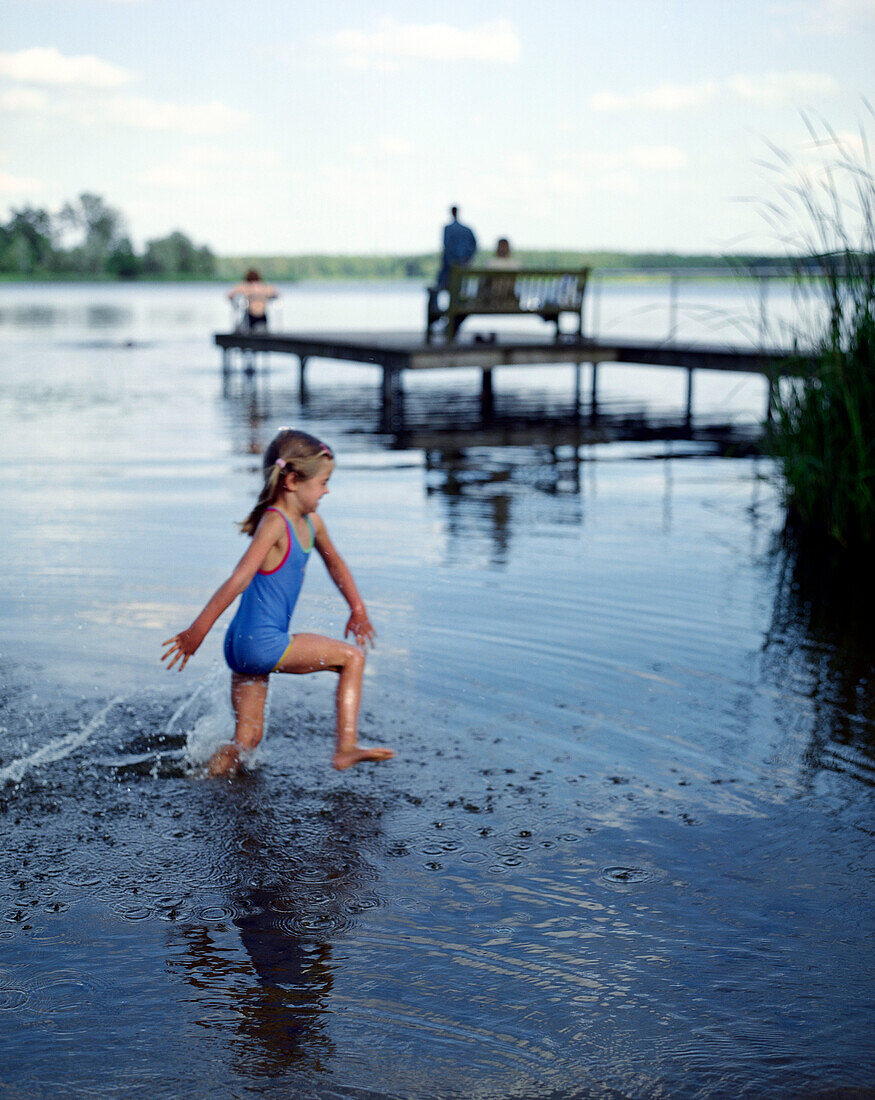 Girl (5 years) walking throug water at lakeshore, Lake Neukloster, Nakenstrof, Mecklenburg-Western Pomerania, Germany