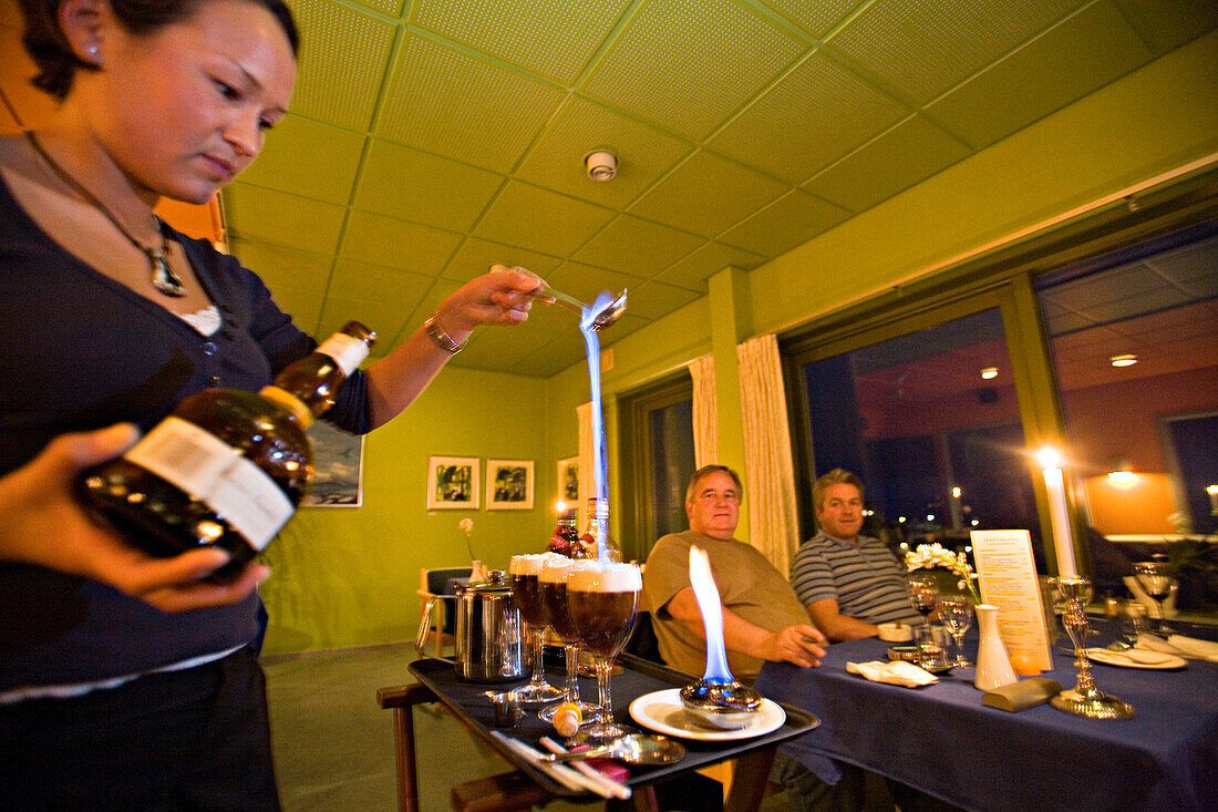 Eine Kellnerin serviert einen Grönland Kaffee. Der brennende Alkohol symbolisiert das Polarlicht, der Rahm das Eis und der Kaffee den Boden, Qaqortoq (ehem. Julianehab), Süd Grönland.