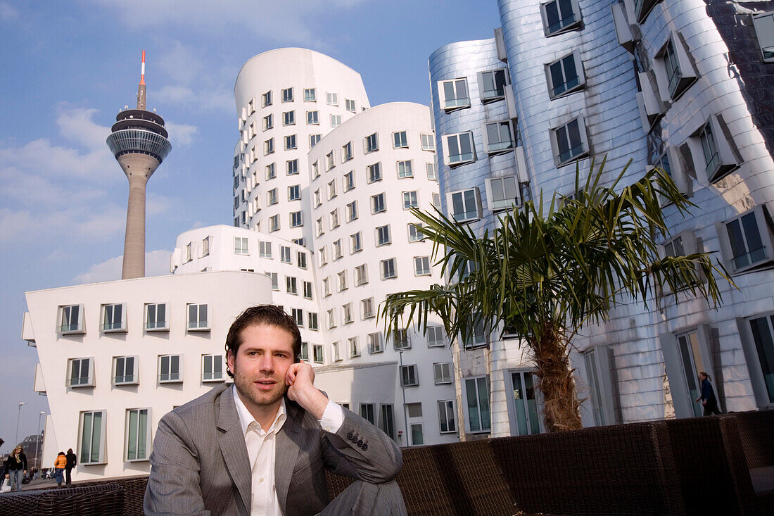Junger Mann telefoniert vor Neuer Zollhof, Architektur von Frank O.Gehry, mit Fernsehturm, Rheinturm im Hintergrund, Medienhafen in Düsseldorf, Nordrhein-Westfalen, Landeshauptstadt in NRW, Deutschland