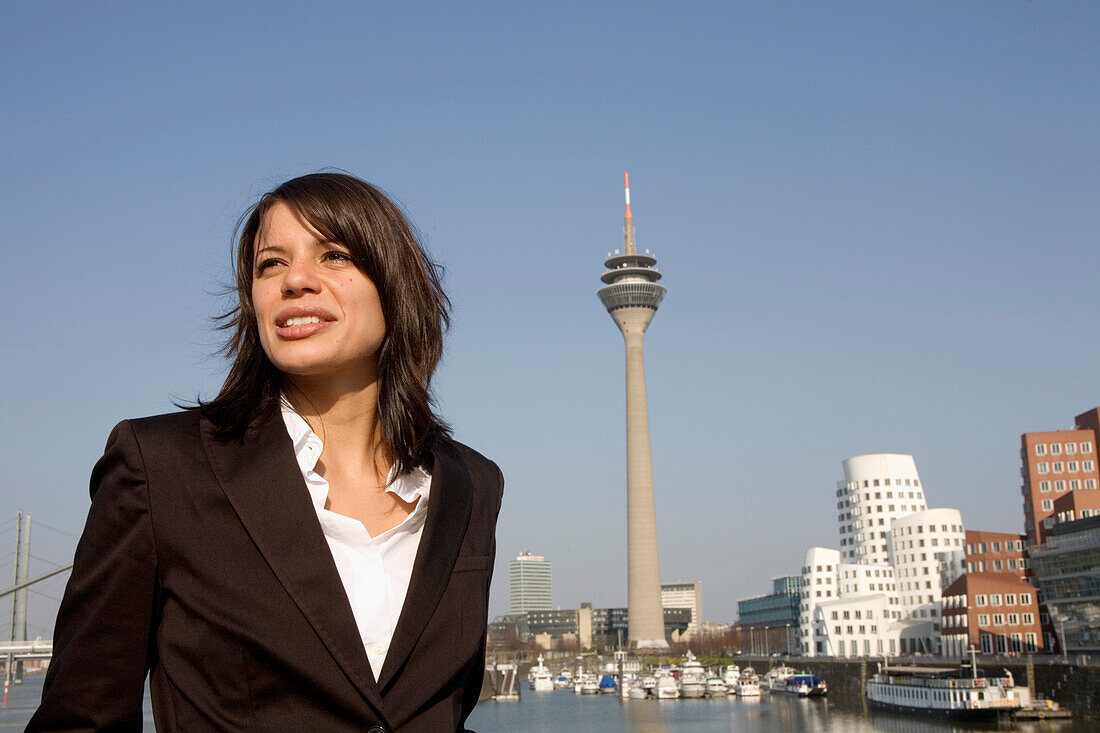 Young business woman in front of city skyline with television tower, Neuer Zollhof in the background, Media Harbour, architecture from Frank O.Gehry, Düsseldorf, state capital of NRW, North-Rhine-Westphalia, Germany