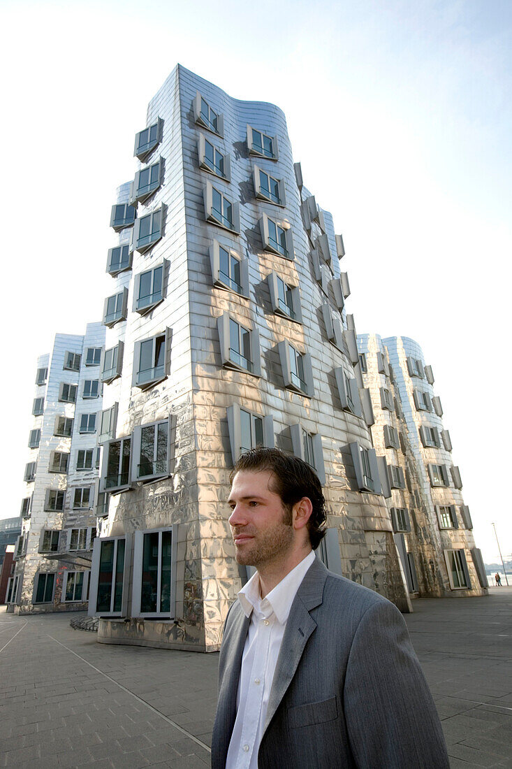 Young business man in front of Neuer Zollhof, modern architecture from Frank Gehry, Media Harbour, Düsseldorf, state capital of NRW, North-Rhine-Westphalia, Germany