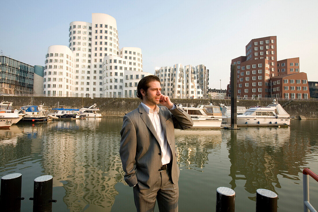 Young business man taking on a mobile phone, modern architecture from Frank Gehry, office buildings, Media Harbour, Neuer Zollhof, Düsseldorf, state capital of NRW, North-Rhine-Westphalia, Germany