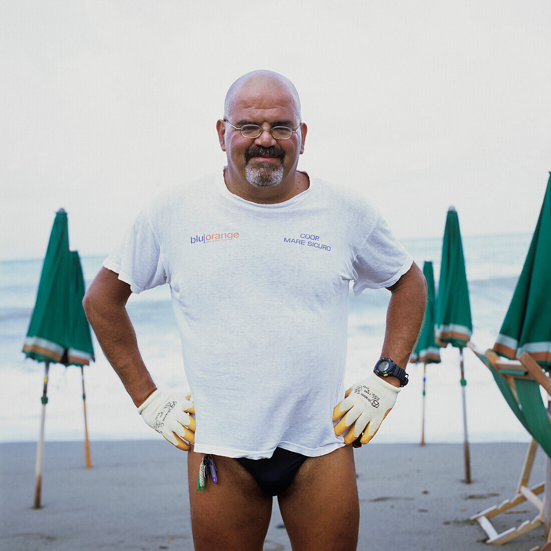 bath attendant in Levanto, Ligurien, Italy, wearing gloves, security, working, to position deckchais, to put away deckchairs, putting his hands in his hips, smiling in Camera, friendly, looking for, closing time, end of work, after work, finish, glasses, 