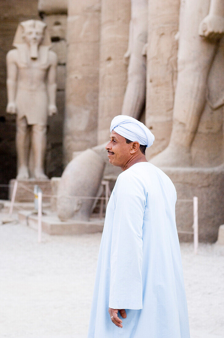 An Egyptian standing next to statues in Luxor Temple, Luxor, Egypt