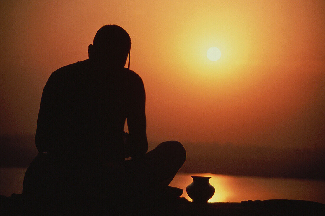 Silouette of a man praying with vase, India