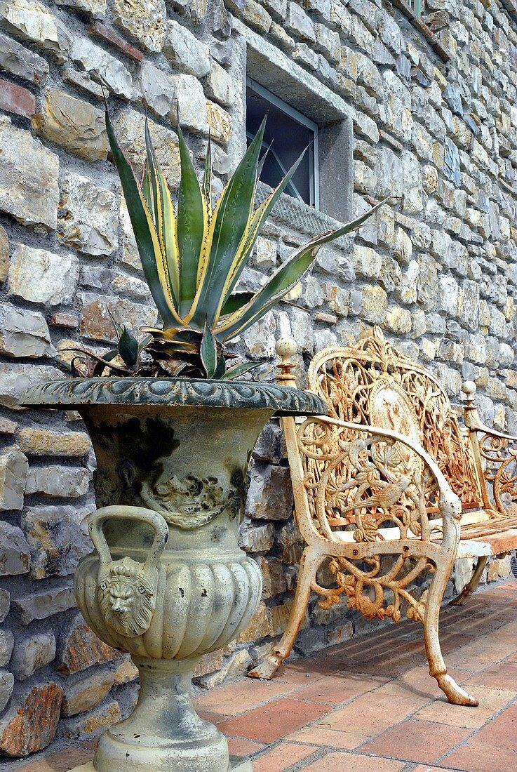 Agave im antiken Gefäss und rostige Sitzbank vor Natursteinfassade