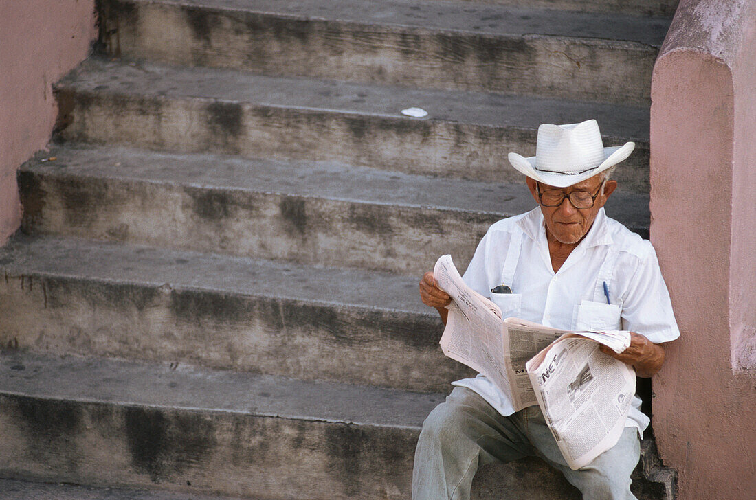 Mexican man sitting on the steps and reading a newspaper, Market, Merida, Yucatan Peninsula, Mexico