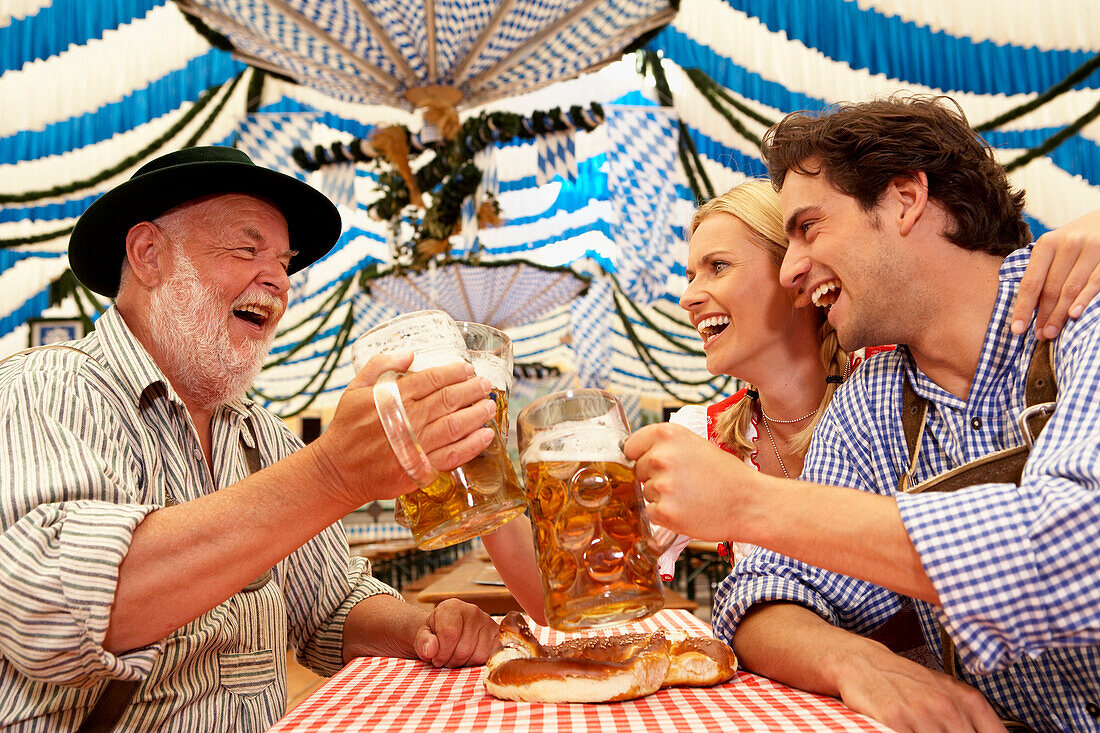 Paar und ein älterer Mann stoßen mit Bier im Bierzelt an