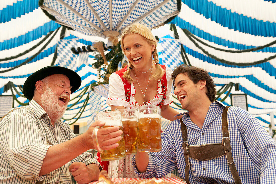 Paar und ein älterer Mann stoßen mit Bier im Bierzelt an
