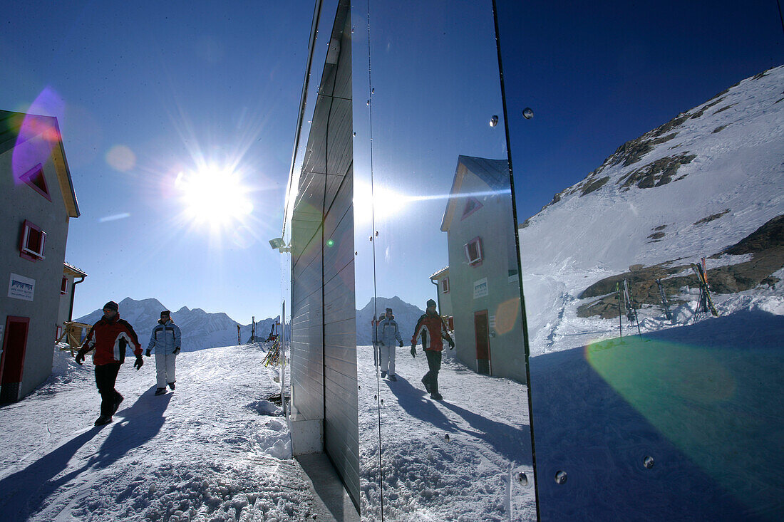 Reflection of skiers and alpine hut Bella Vista on facade, Schnals valley, South Tyrol, Italy
