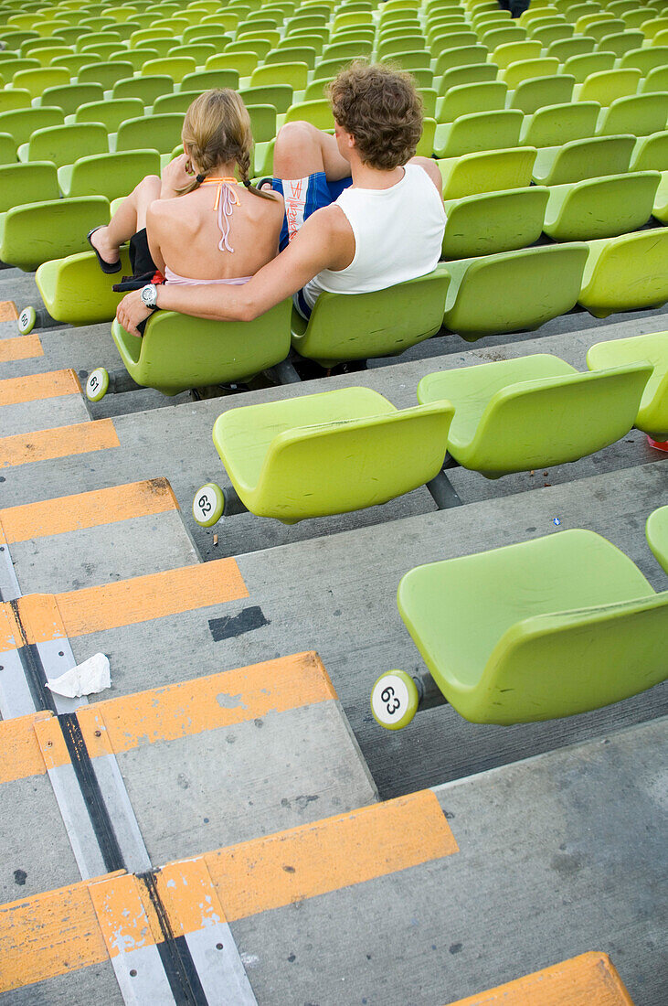 Young couple sitting on the bleachers of Munich's Olympic Stadium, Munich, Bavaria, Germany