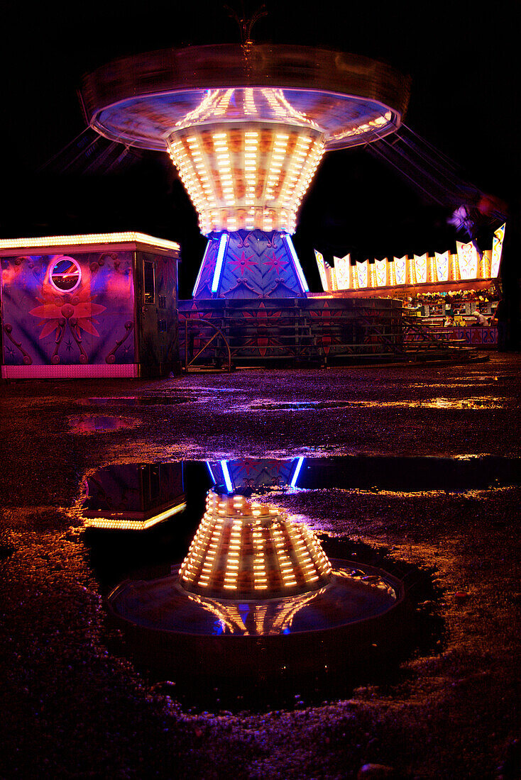 Reflection of chain swing ride in a puddle at night, Kaufbeuren, Bavaria, Germany