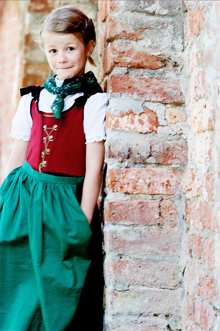 Girl wearing dirndl dresses leaning against wall, Irsee, Bavaria, Germany
