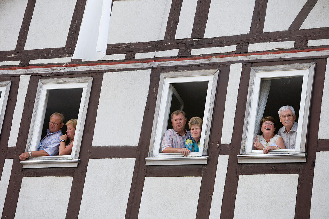 Spectators looking out through windows of a timberframe house, Schlitz International Festival, Schlitzerlaender Trachten- und Heimatfest, Schlitz, Vogelsberg, Hesse, Germany