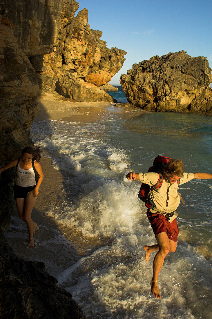 A couple jumping over the waves on a beach, Madagascar, Africa