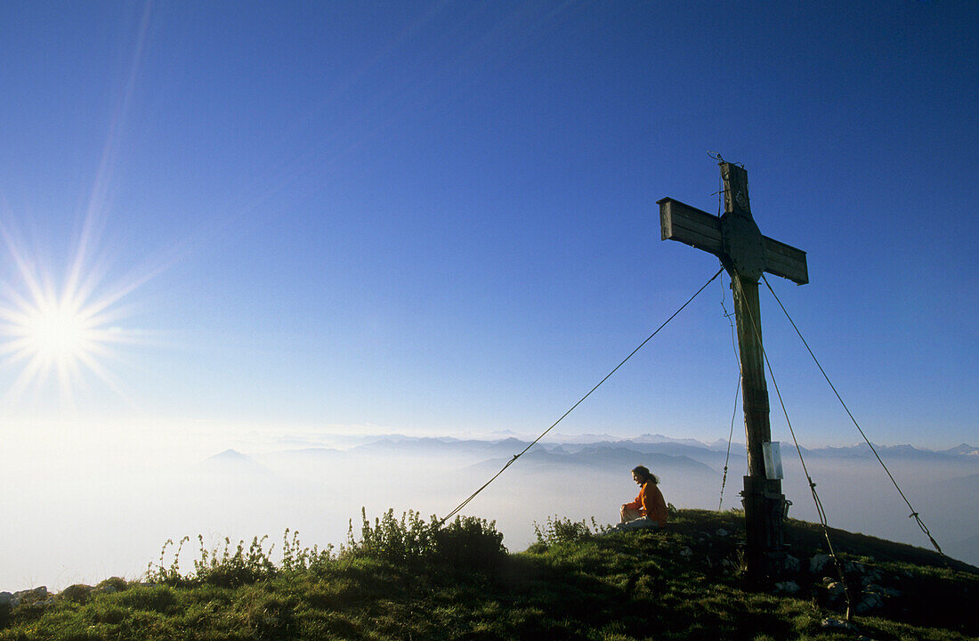 Hiker resting near summit cross of Sonnwendjoch, Rofan range, Tyrol, Austria