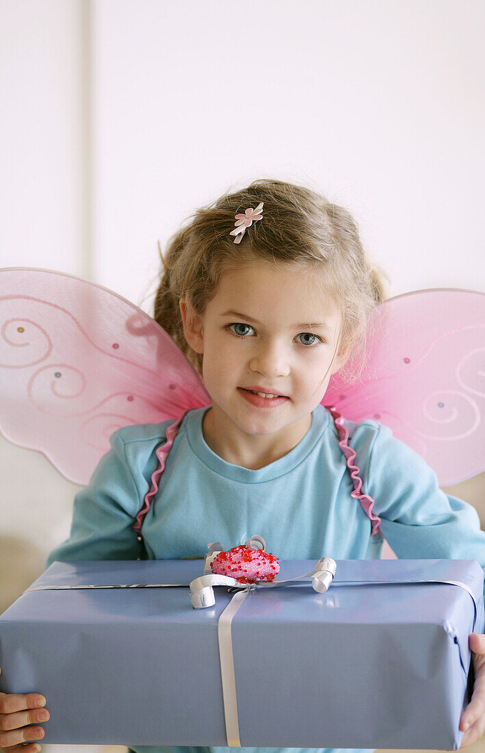 Mädchen (3-4 Jahre) mit Schmetterlingsflügeln hält ein Geschenk