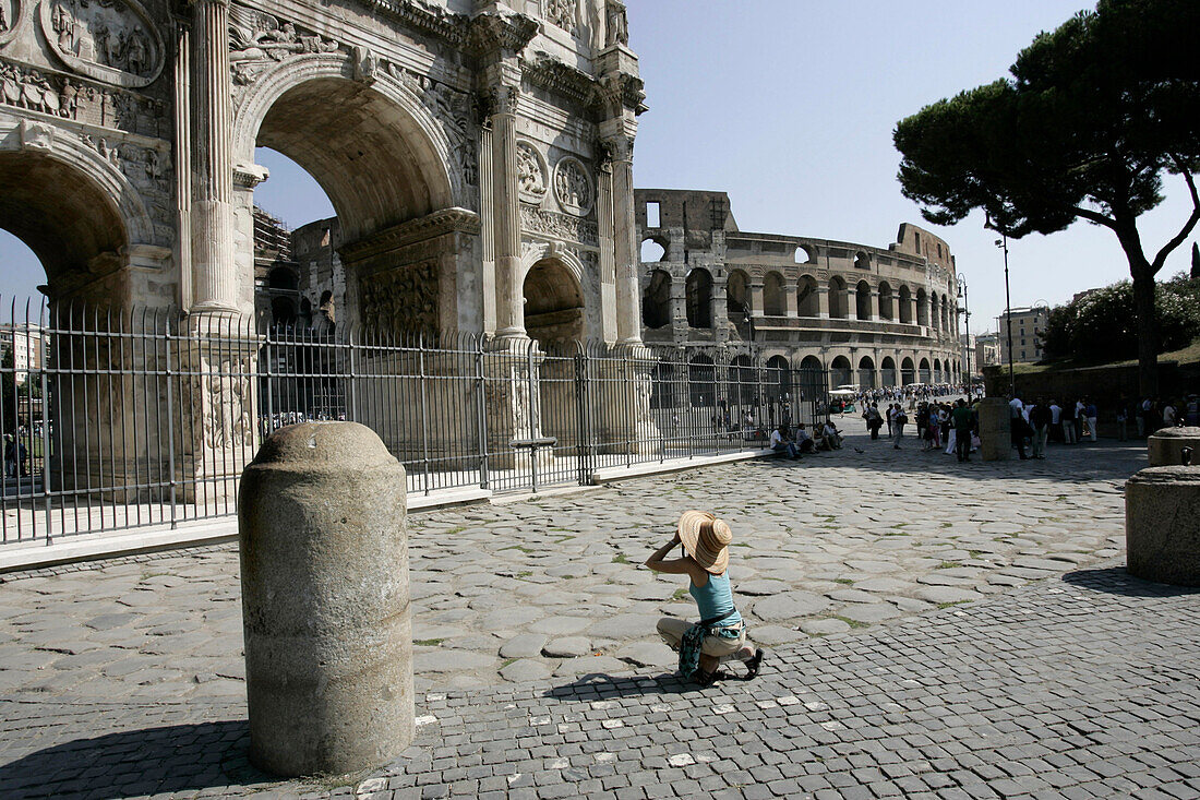 Tourist kneeling down with camera at the Arch of Constantine, Colosseum in the background, Rome, Italy