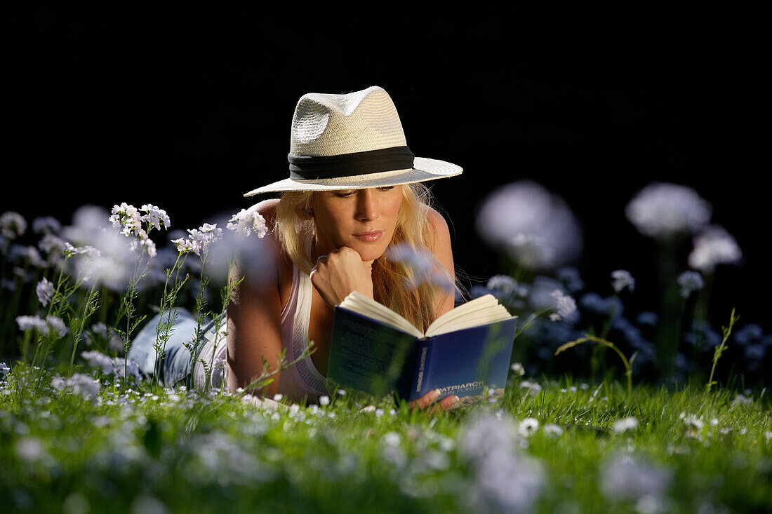 Junge Frau liegt auf einer Wiese und liest ein Buch, Icking, Bayern, Deutschland