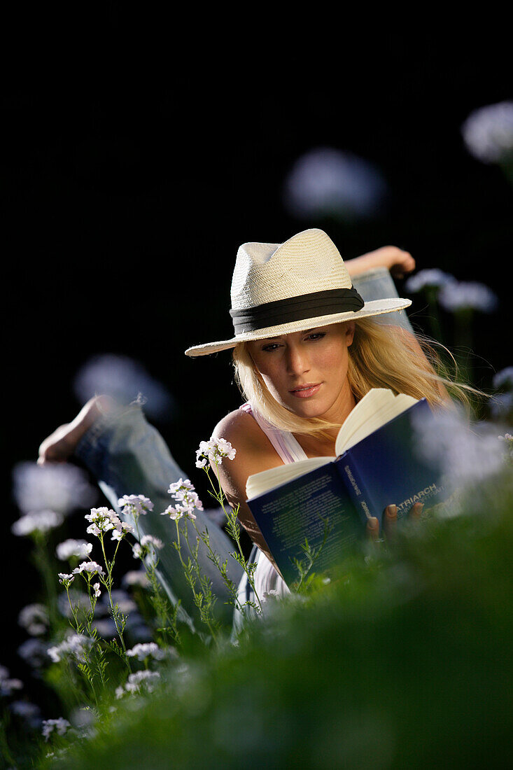 Junge Frau liegt auf einer Wiese und liest ein Buch, Icking, Bayern, Deutschland