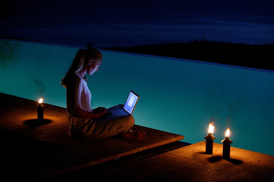 Junge Frau sitzt mit Laptop am Pool, nahe Uluwatu, Bali, Indonesien