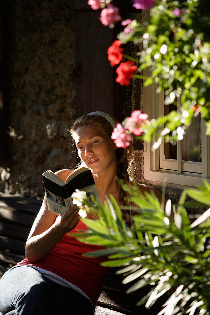 Junge Frau sitzt vor einem Haus und liest ein Buch, Brannenburg, Oberbayern, Bayern, Deutschland