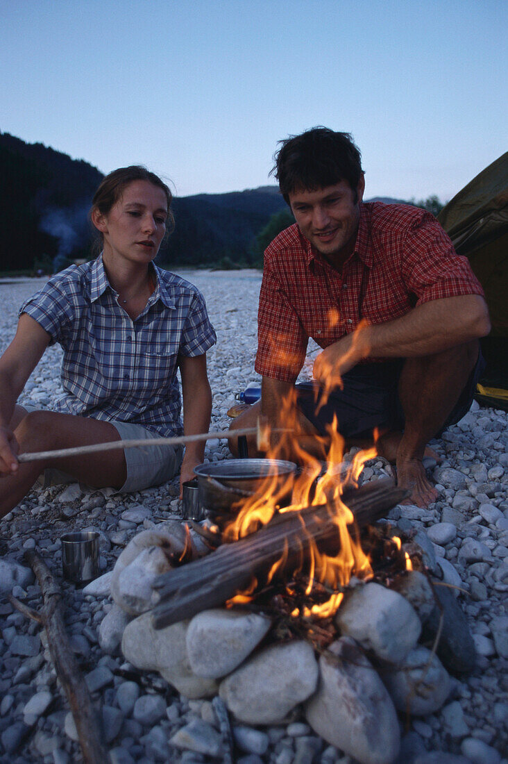 Couple sitting at campfire, Sylvenstein lake, Bavaria, Germany