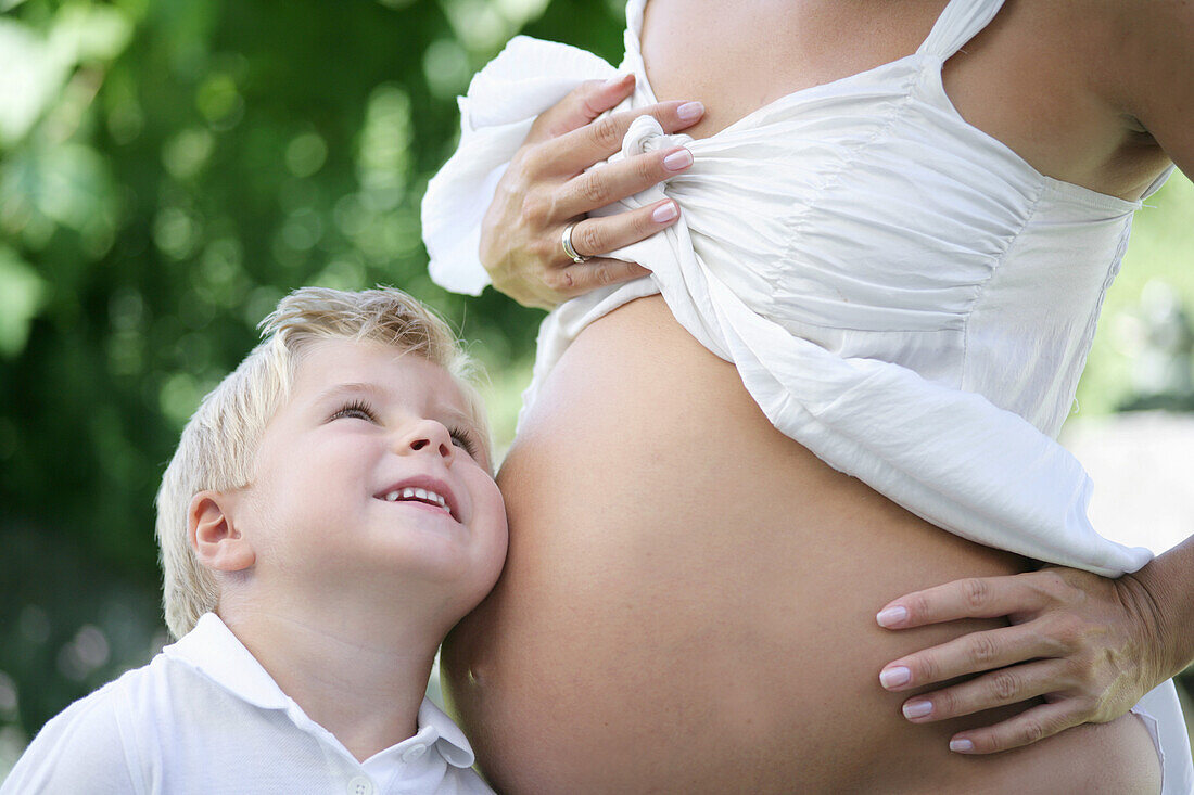 Junge (4-5 Jahre) legt sein Ohr an Babybauch seiner Mutter, Steiermark, Österreich