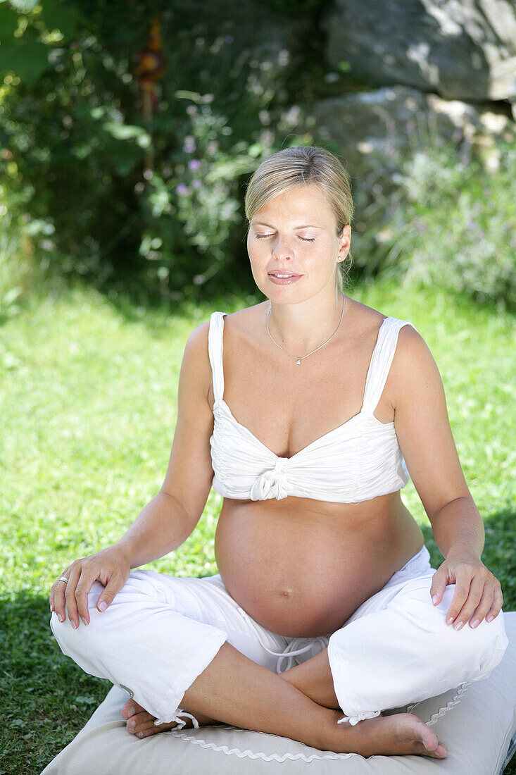 Pregnant woman meditating, sitting on grass, Styria, Austria