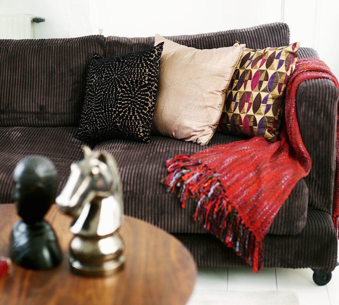 Braunes Kordsofa mit Kissen und roter Tagesdecke