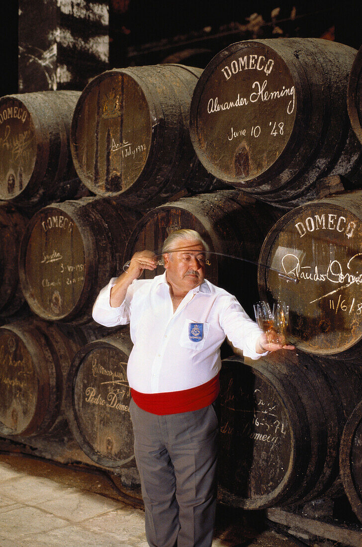 Ein Weinprüfer gießt Sherry in Probiergläser vor einem Stapel Sherry Fässer, Faßkeller der Bodegas Pedro Domeq, Jerez de la Frontera, Provinz Cádiz, Andalusien. Spanien