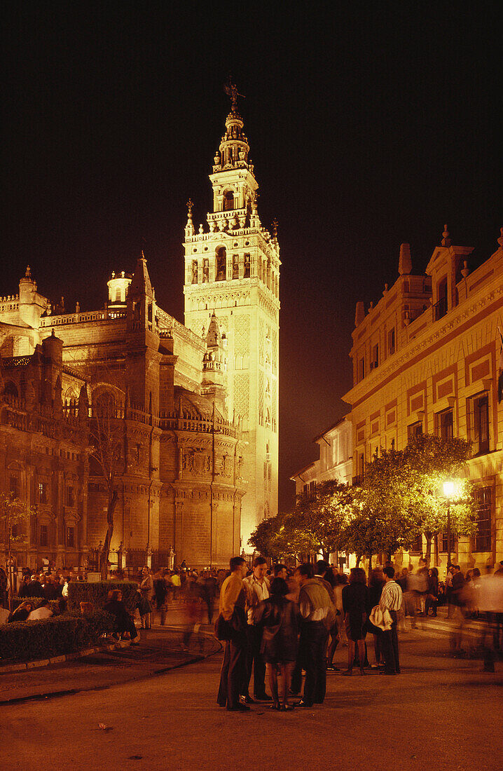 Menschen stehen abends vor dem beleuchteten Glockenturm der Kathedrale Santa Maria de la Sede, Plaza Triunfo, Sevilla, Andalusien, Spanien