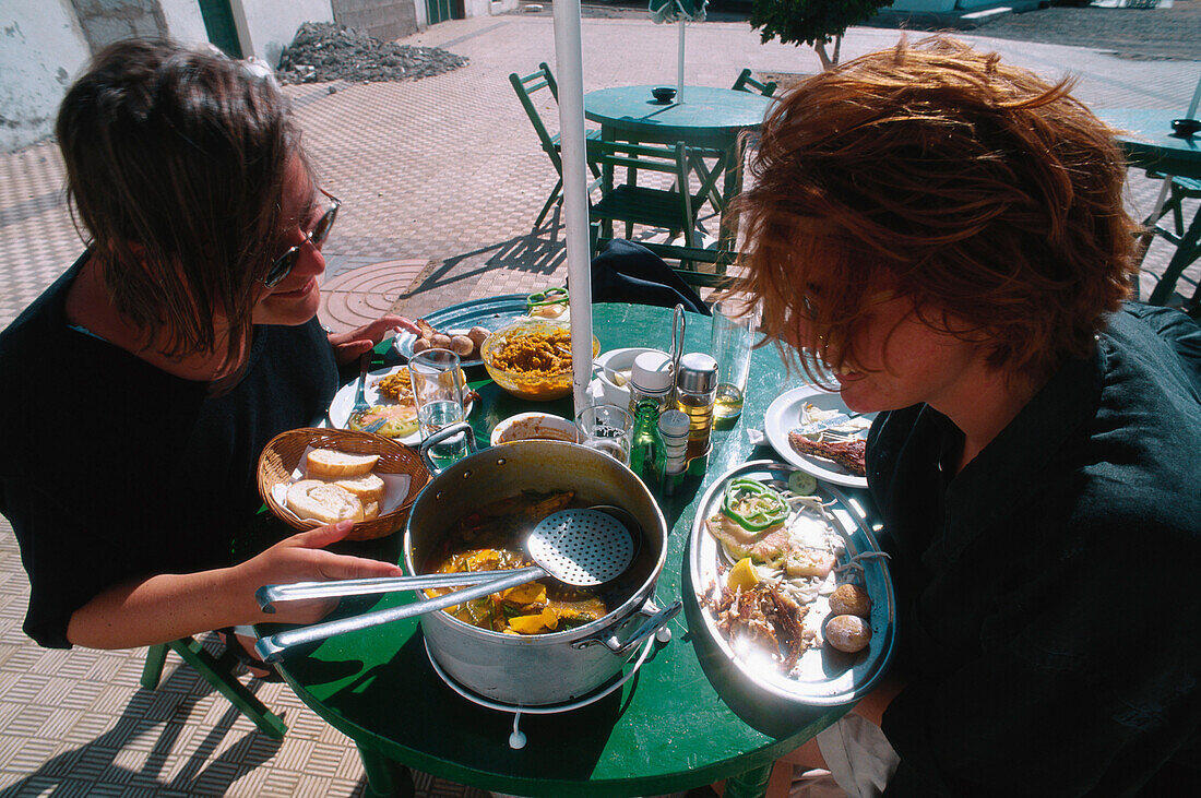 Zwei Frauen essen ein Fischgericht vor einer Bar in Puerto de la Luz, Jandia Halbinsel, Fuerteventura