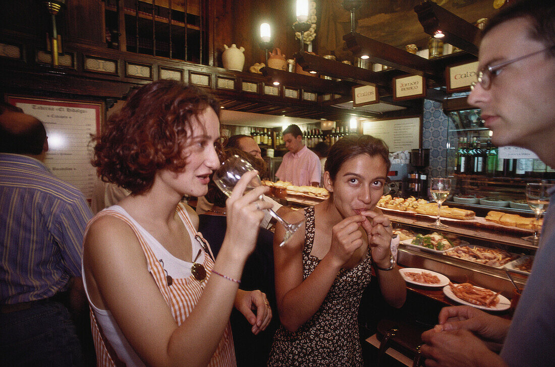 Two young women and a young man drinking wine and tasting some tapas from the counter in a bar in Valladolid, Castilla-Leon, Northern Spain