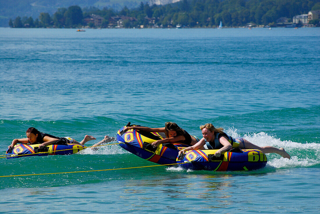 drei junge Frauen beim Tube Riding hinter dem Motorboot, Abersee, Wolfgangsee, Salzkammergut, Salzburg, Österreich