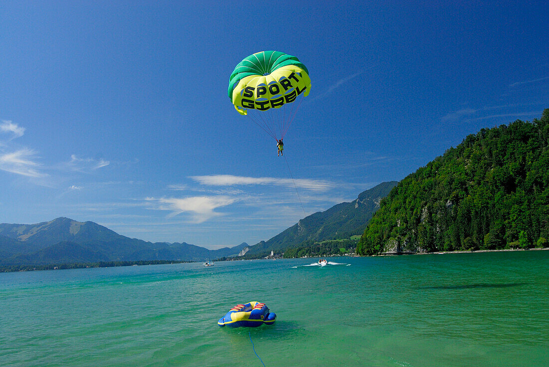 young woman parasailing behind motor boat, lake Abersee, lake Wolfgangsee, Salzkammergut, Salzburg, Austria