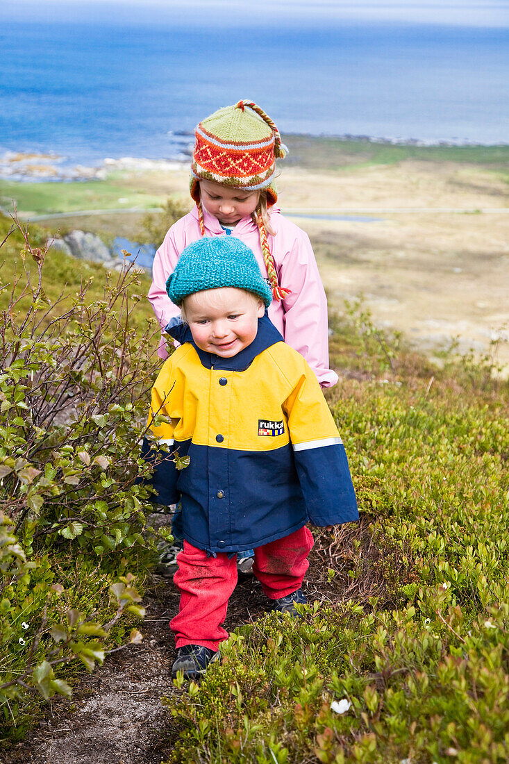 Two small girls, children, in raincoats walking along the beach, Gimsoya Island, Lofoten, Norway