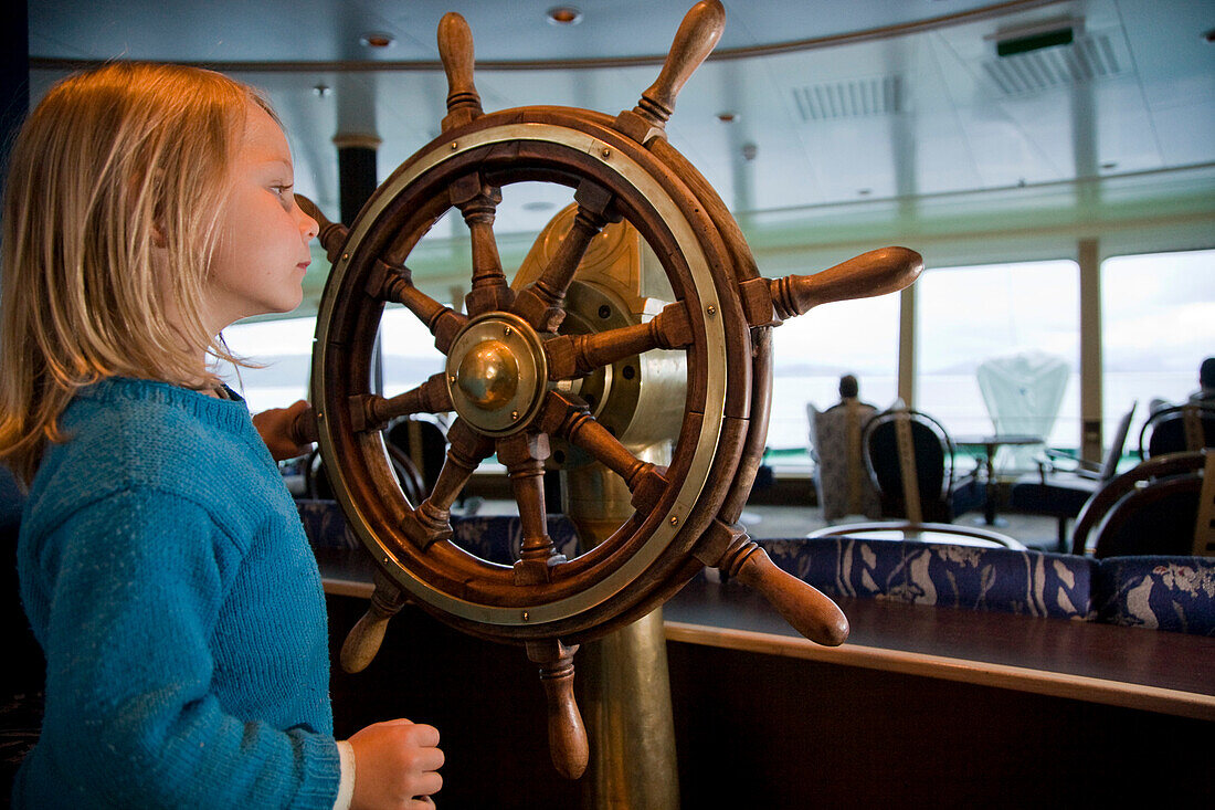 Kleines Mädchen spielt mit einem Schiffssteuerrad an Bord eines Hurtigruten Postschiffes, Norwegen, MR.