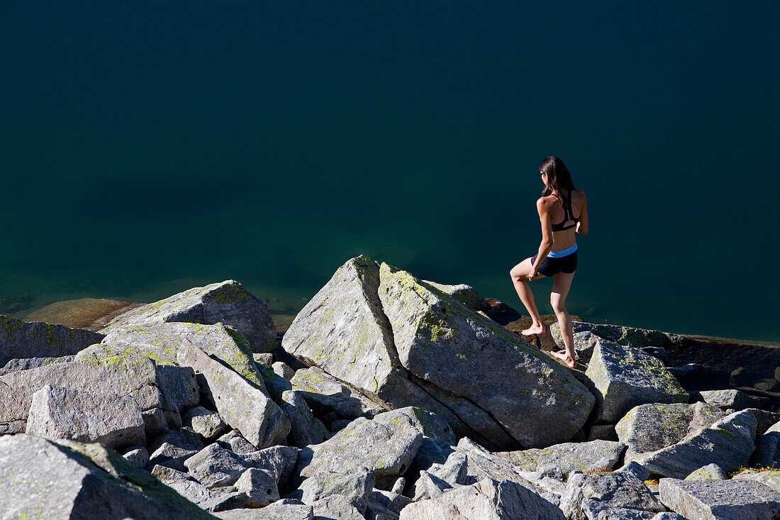 Young woman standing on rock at lake Laghi d'Orsirora, Gotthard, Canton of Ticino, Switzerland