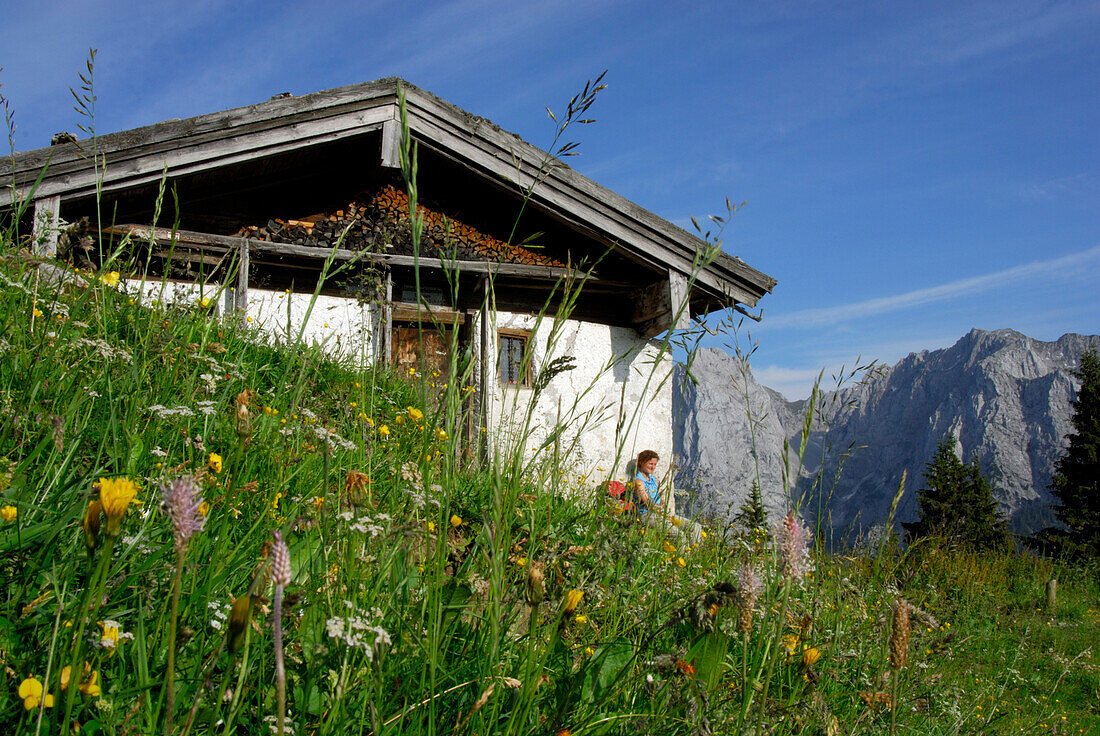 Wanderin sitzt vor Hütte, Hinterkaiserfeldenalm mit Blick auf den Wilden Kaiser, Kaisergebirge, Tirol, Österreich